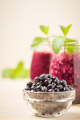 Blueberry smoothie decorated with fresh green mint leaves and raw ripe berries on yellow pastel background.