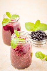 Blueberry smoothie decorated with fresh green mint leaves and raw ripe berries on yellow pastel background.
