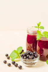 Currant smoothie decorated with fresh green mint leaves and raw ripe berries on yellow pastel background.