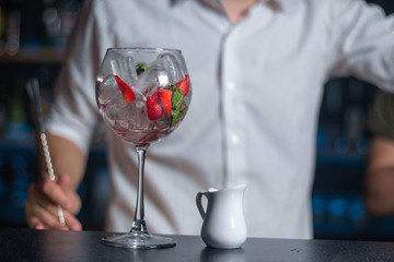 Wine glass filled with ice, strawberries and mint, and white milk pitcher on the bar counter.