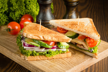 Close-up of two sandwiches with bacon, salami, prosciutto and fresh vegetables on rustic wooden...