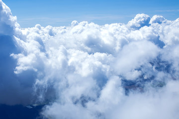 Airplain window seat view of big white thick fluffy clouds with a clear blue sky at the background