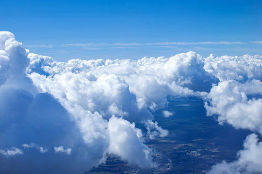 Airplain window seat view of big white thick fluffy clouds with a clear blue sky at the background