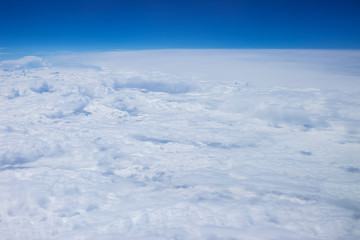 Fototapeta na wymiar Airplain window seat view of big white thick fluffy clouds with a clear blue sky at the background