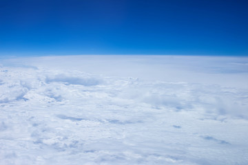 Airplain window seat view of big white thick fluffy clouds with a clear blue sky at the background