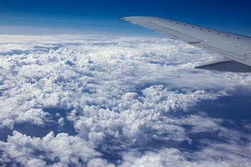 Fototapeta na wymiar Airplain window seat view of big white thick fluffy clouds with a clear blue sky at the background