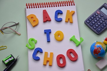 Back to school. Items for the school on a green table. inscription in colored letters back to school. notebook, notebook, ruler, eraser, pencil, pen, pen, compasses, globe, calculator glasses.