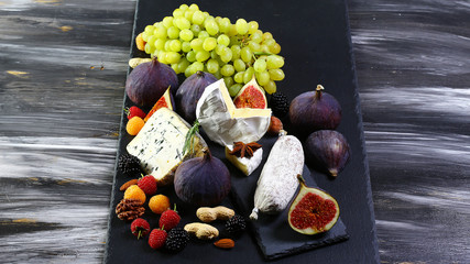 Set snacks for wine on a shale board: cheese camembert or brie cheese, cheese Dor blue with figs,...