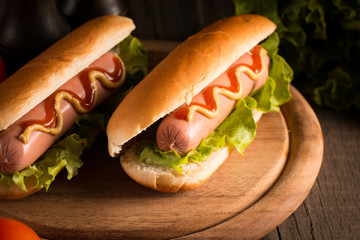Photo of barbecue grilled hot dog with yellow mustard and ketchup on wooden background. Hot dog sandwich with potato fries and sauces.