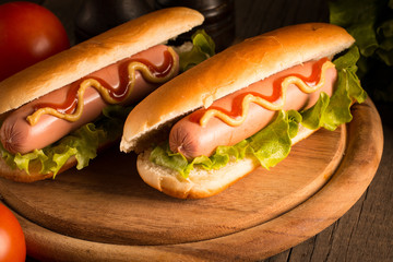 Photo of barbecue grilled hot dog with yellow mustard and ketchup on wooden background. Hot dog sandwich with potato fries and sauces.