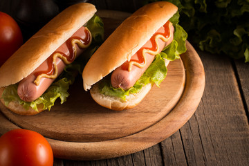 Photo of barbecue grilled hot dog with yellow mustard and ketchup on wooden background. Hot dog sandwich with potato fries and sauces.