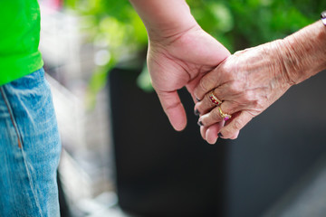 wrinkled elderly woman's hand holding to young man's hand, walking in shopping mall park. Family Relation, Health, Help, Support, Insurance concept.