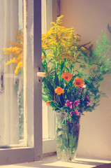 A bouquet of different wildflowers stands on the windowsill. Toning in the style of instagram.
