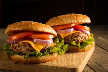 Home made hamburger with beef, onion, tomato, lettuce and cheese. Fresh burger close up on wooden rustic table with potato fries, beer and chips. Cheeseburger.