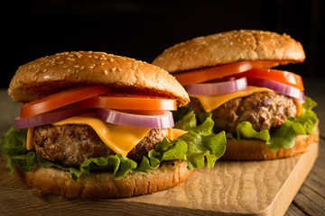 Home made hamburger with beef, onion, tomato, lettuce and cheese. Fresh burger close up on wooden rustic table with potato fries, beer and chips. Cheeseburger.