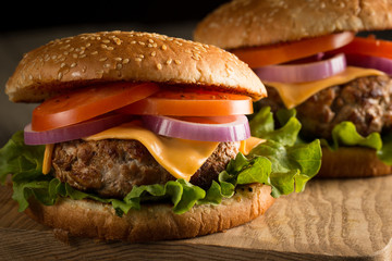 Home made hamburger with beef, onion, tomato, lettuce and cheese. Fresh burger close up on wooden rustic table with potato fries, beer and chips. Cheeseburger.