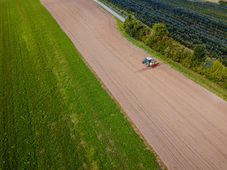 Aerial view of tractor on farmland spraying fertilizer on a brown field.