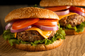 Home made hamburger with beef, onion, tomato, lettuce and cheese. Fresh burger close up on wooden rustic table with potato fries, beer and chips. Cheeseburger.