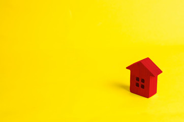 Fototapeta na wymiar A small red wooden house stands on a yellow background. The concept of buying and selling real estate, renting. Search for a house. Affordable housing, credit and loans. Investments in business