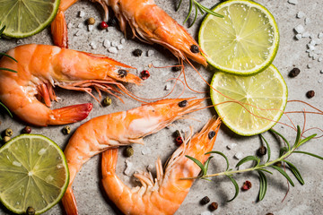 Tiger shrimps with lime, lemon, rosemary and black pepper spices on stone background. Fresh tasty prawns ready to be cooked