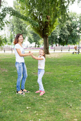 Obraz premium daughter and mother spinning on the lawn.in a white t-shirt and jeans. a walk in the Park. child. mother-daughter. summer.