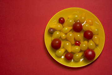 Yellow and red cherry tomatoes on yellow plate red background. Organic food