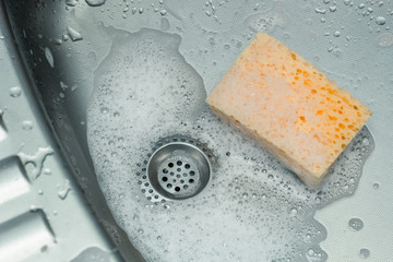View of a sink, drain and flowing water with a sponge in the foam. 