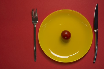 Diet concept plate top view. Cherry tomato on yellow empty plate with fork and knife on red background