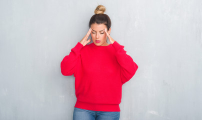 Young adult woman over grey grunge wall wearing winter outfit with hand on head for pain in head because stress. Suffering migraine.