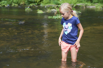 Child cute blond girl playing in the creek. Girl walking in forest stream and exploring nature. Summer children fun. Children summer activities