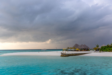 An idyllic island in Maldive in a stormy weather afternoon. Super clear water, white sand, traditional huts and tropical climate feeling.