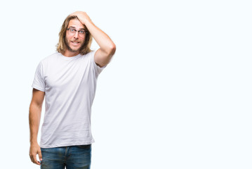 Young handsome man with long hair wearing glasses over isolated background surprised with hand on...