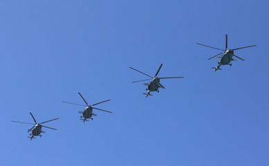 Several military helicopters fly side by side against the blue sky