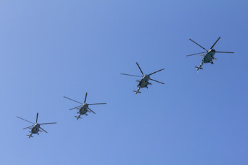 Several military helicopters fly side by side against the blue sky