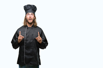 Young handsome cook man with long hair over isolated background amazed and surprised looking up and...