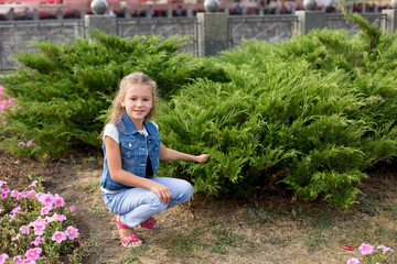 a little girl sitting on a flower bed among the flowers and . girl in a white t-shirt and jeans. a walk in the Park. child