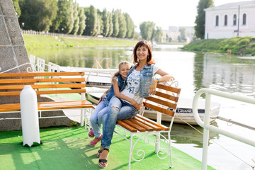 Fototapeta na wymiar little girl and mom sitting on a bench by the river. girl in a white t-shirt and jeans. a walk in the Park. child