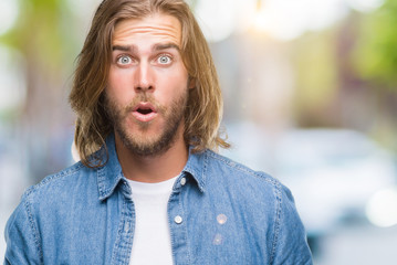 Young handsome man with long hair over isolated background afraid and shocked with surprise...