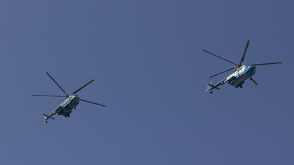 Several military helicopters fly side by side against the blue sky