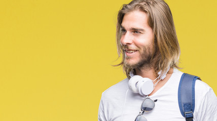 Young handsome tourist man with long hair wearing backpack over isolated background looking away to...