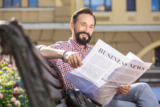 Delighted adult man reading a newspaper with pleasure