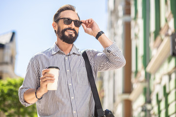 Joyful bearded man drinking coffee on the street