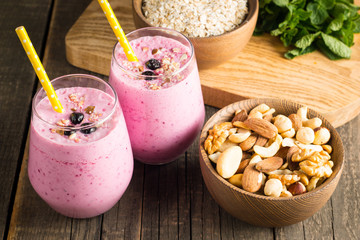 Glasses of berry smoothie with nuts, mint, blueberry, blackberry, raspberry, and yogurt on wooden table. Weight loss and diet concept. 
