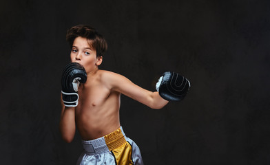 Fototapeta na wymiar Handsome shirtless young boxer during boxing exercises, focused on process with serious concentrated facial. Isolated on the dark background.