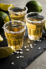Macro photo of shots of gold Mexican tequila with lime and salt on wooden rustic background....