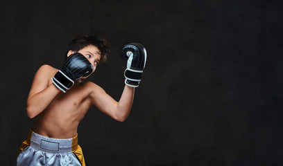 Handsome shirtless young boxer during boxing exercises, focused on process with serious concentrated facial. Isolated on the dark background.