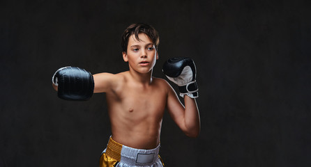 Fototapeta na wymiar Handsome shirtless young boxer during boxing exercises, focused on process with serious concentrated facial. Isolated on the dark background.