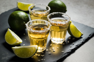 Macro photo of shots of gold Mexican tequila with lime and salt on wooden rustic background....
