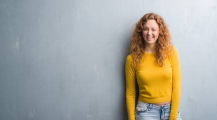 Fototapeta premium Young redhead woman over grey grunge wall winking looking at the camera with sexy expression, cheerful and happy face.