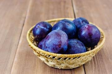 plum in a wicker basket on a wooden table